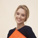 smiling woman standing while holding orange folder